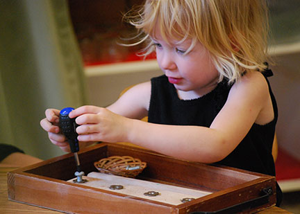 A child works with screws and a screwdriver in the primary program.